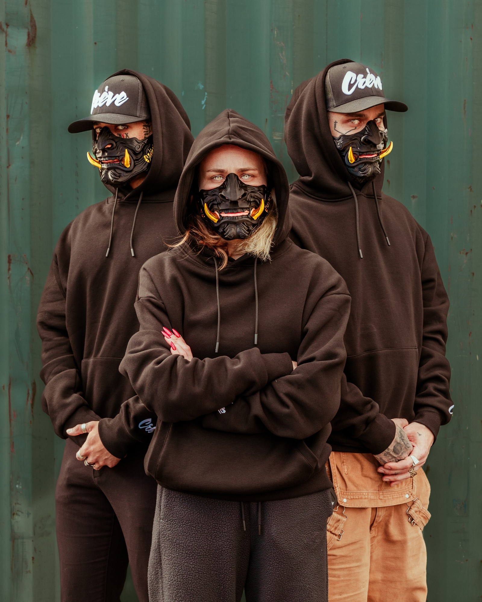 Équipe Crève en sweats noirs et masques oni devant un décor industriel